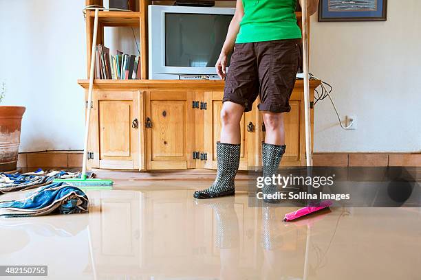 hispanic woman sweeping water out of flooded house - flooded home stock-fotos und bilder