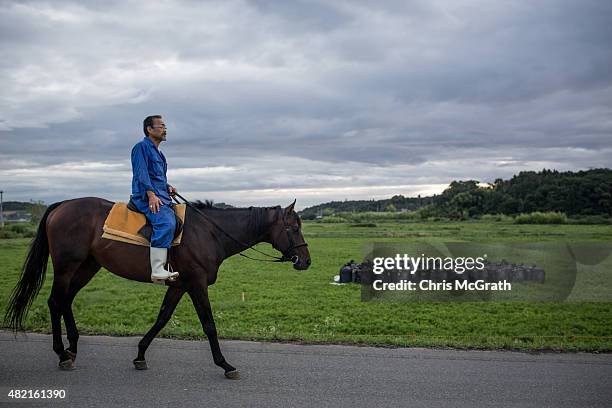 Horseman rides past bags of radiated soil left on the side of the road while taking his horse out for a training session ahead of the Soma Nomaoi...