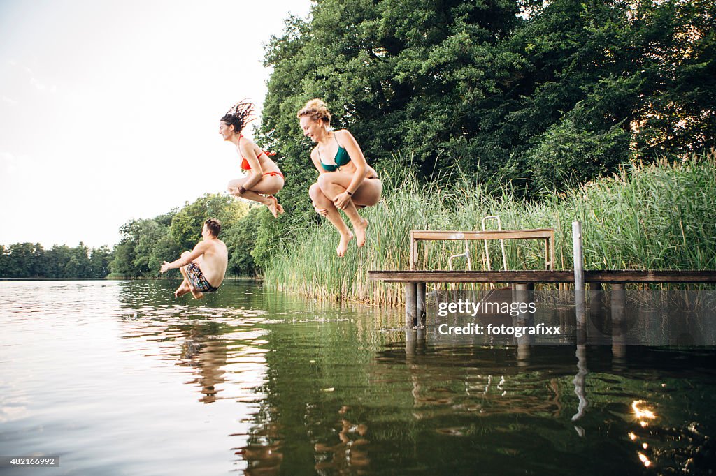 Summer day: three young adults jump from jetty into lake