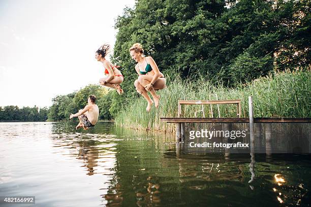 summer day: three young adults jump from jetty into lake - swimming stock pictures, royalty-free photos & images