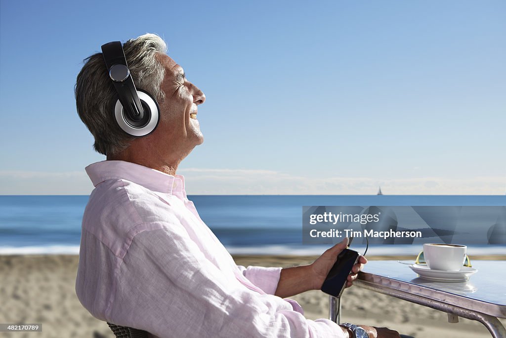 Senior man listening to music with headphones on beach