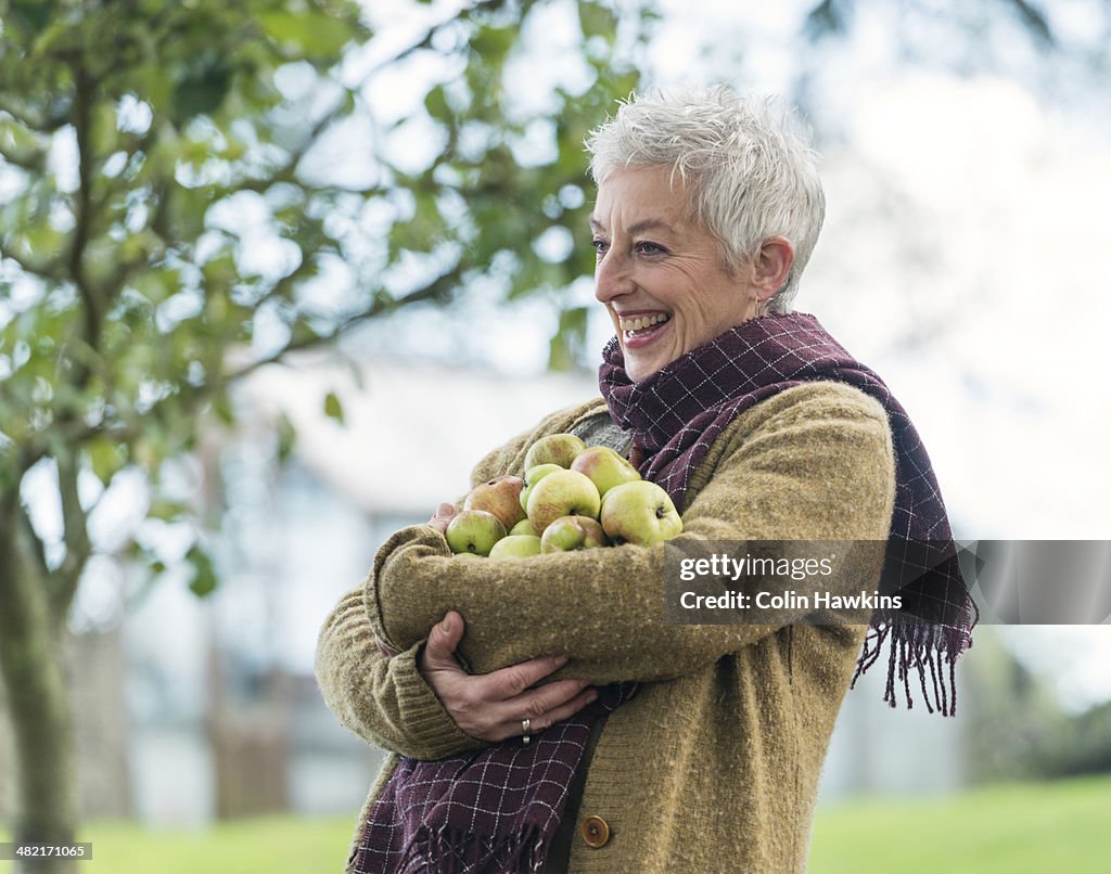Happy senior woman with armful of apples