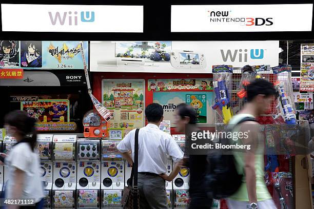 Pedestrians walk past signage for Nintendo Co.'s new 3DS handheld game players, top right, and Wii U game consoles displayed outside an electronics...