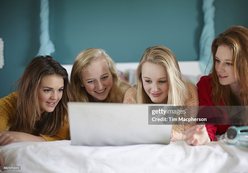 Four teenage girls looking at laptop in bedroom