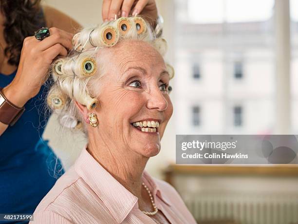 senior woman with rollers at hairdressers - hair curlers stock-fotos und bilder