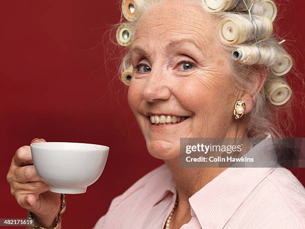 studio portrait of senior woman in hair rollers with cup of tea - curlers stock pictures, royalty-free photos & images