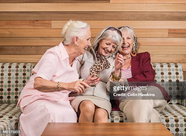 senior women friends laughing on sofa - three people on couch stock pictures, royalty-free photos & images
