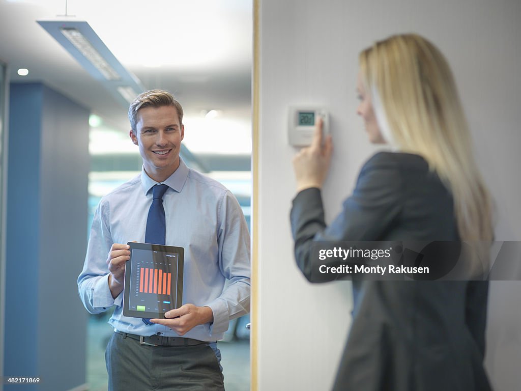 Office workers adjusting heating thermostat and recording information on digital tablet