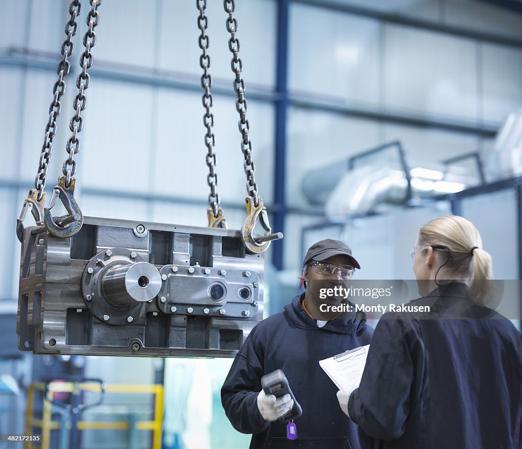 Engineers in discussion next to industrial gearbox in engineering factory
