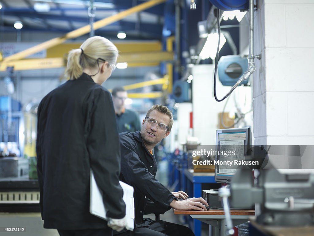 Engineers using computer to work on plans in engineering factory