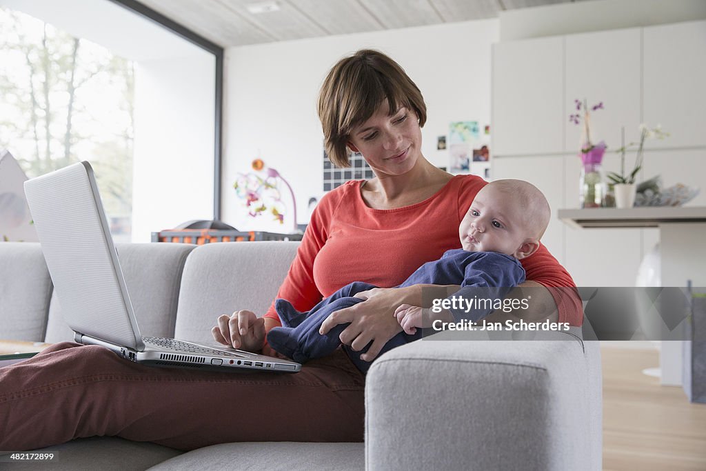 Mother and baby boy reclining on sofa with laptop