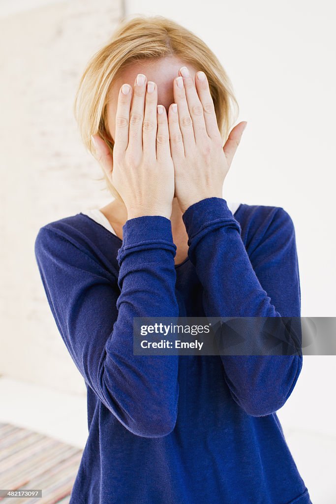 Studio portrait of young woman hiding behind hands