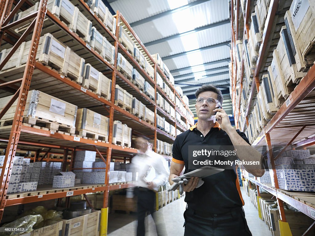 Worker using mobile phone and holding digital tablet in parts store in factory
