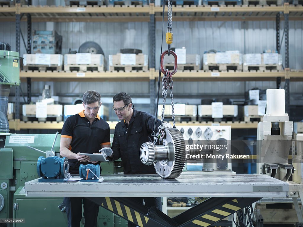 Engineers using digital tablet with gear wheel at work station