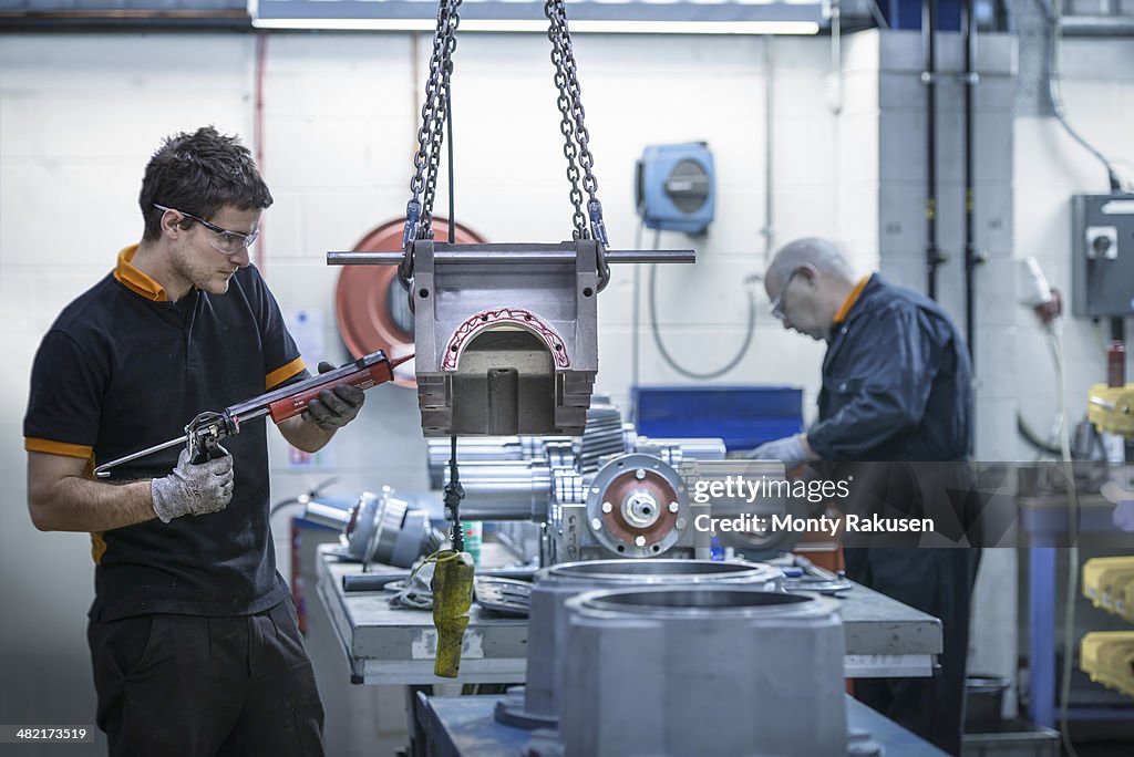 Apprentice engineer applying sealant to industrial gearbox in factory