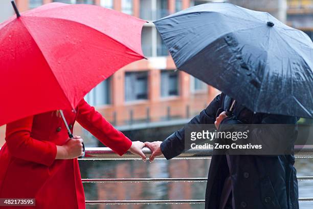 symmetrical couple holding handrail and carrying umbrella's - sharing umbrella stock pictures, royalty-free photos & images