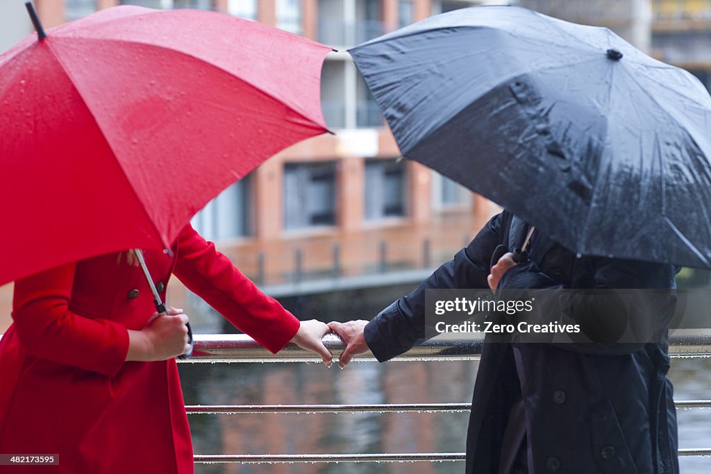 Symmetrical couple holding handrail and carrying umbrella's