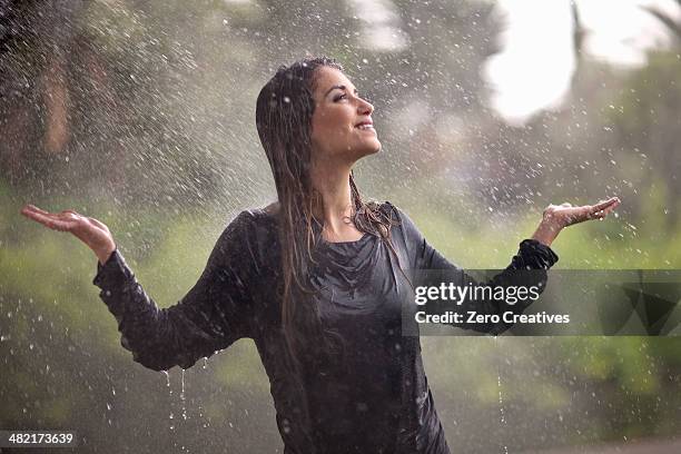 drenched young woman with arms open in rainy park - rain smiling stock-fotos und bilder