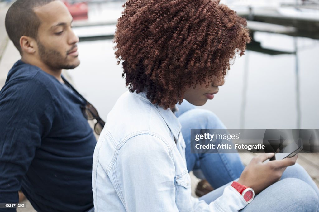 Young woman using cell phone, man watching