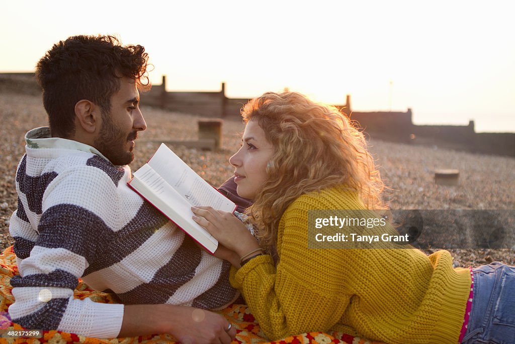 Young couple lying on beach, woman reading book