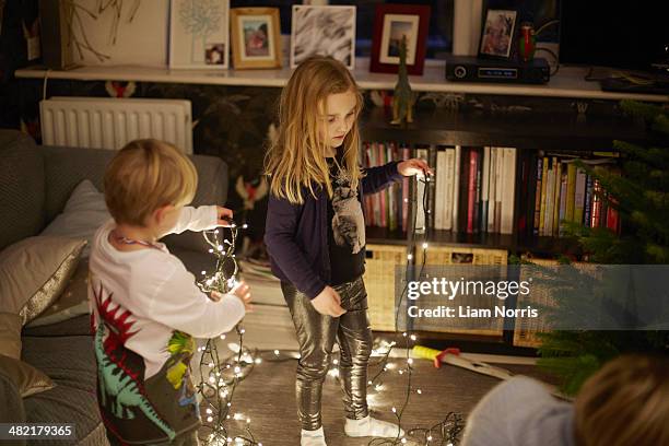 young brother and sister untangling christmas lights - untangle stock-fotos und bilder