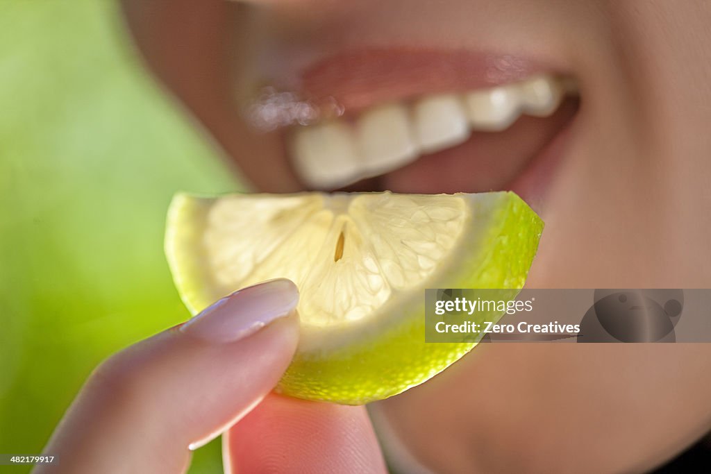 Woman holding slice of lime to mouth