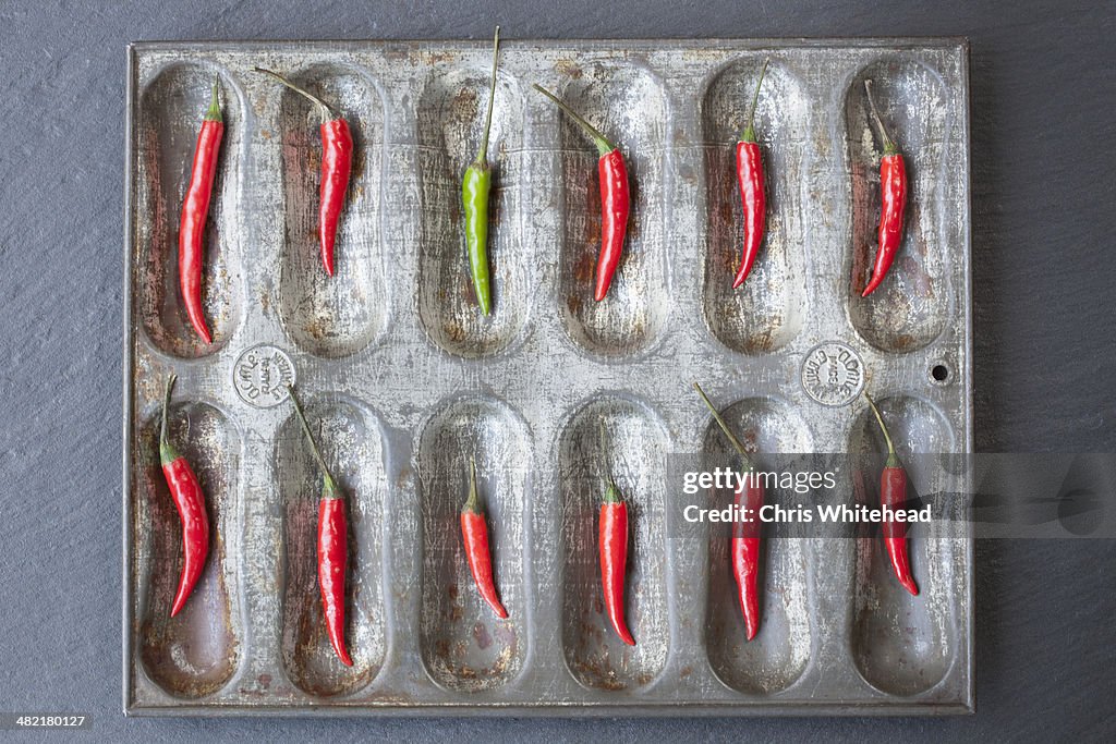 Large group of red chillies and one green chilli ordered in baking tin