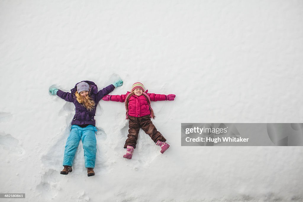 Two sisters playing, making snow angels in snow