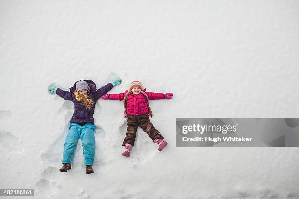 two sisters playing, making snow angels in snow - snow angel stock pictures, royalty-free photos & images