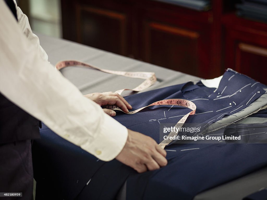 Tailor measuring garment on table in traditional tailors shop