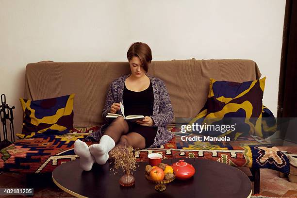 young woman relaxing on sofa reading her book - coffee table front view stock pictures, royalty-free photos & images