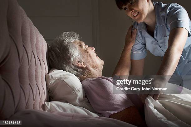 personal care assistant chatting to senior woman in bed - norman elder stock-fotos und bilder