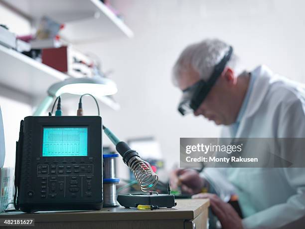 engineer soldering prototype circuit board with oscilloscope in foreground - oscilloscope stock pictures, royalty-free photos & images