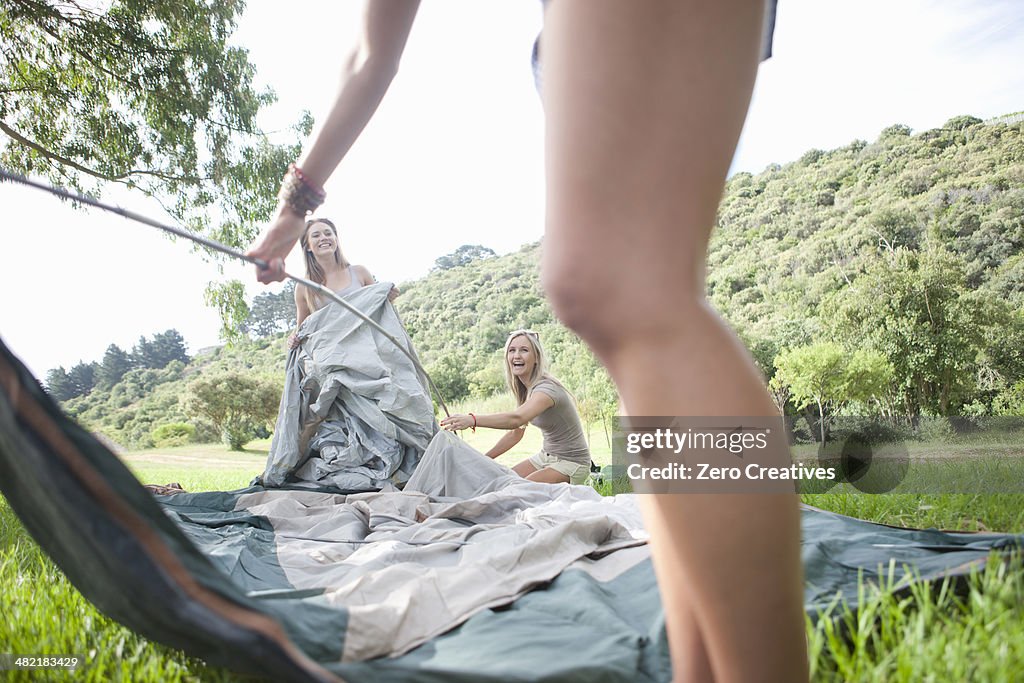 Three friends constructing tent whilst camping