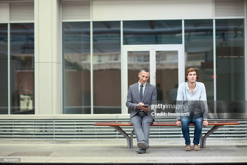 Businessman and young man sitting on train station bench