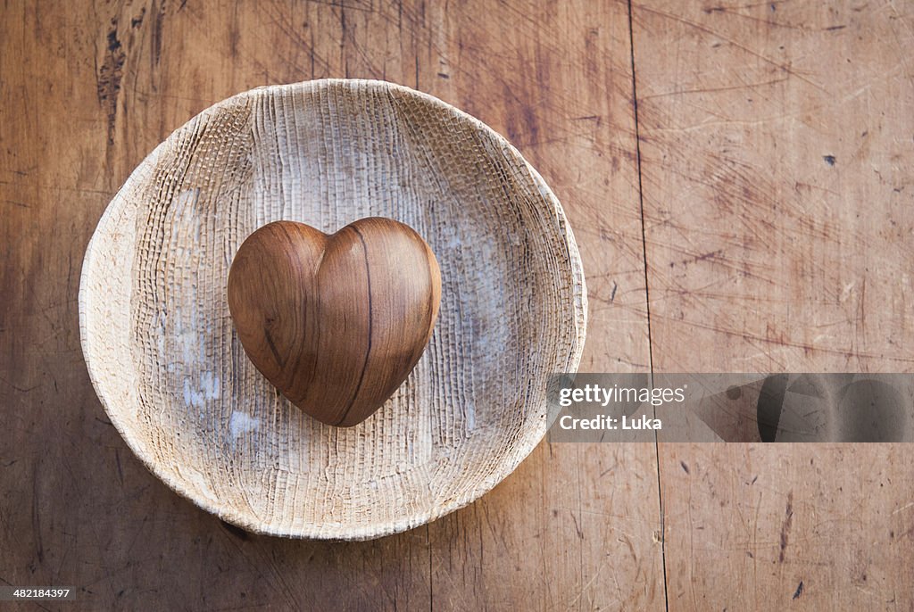 Still life of heart shaped wooden object in wooden bowl