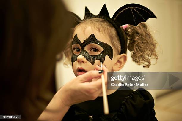 mother painting daughters face for halloween bat costume - pittura per il viso foto e immagini stock