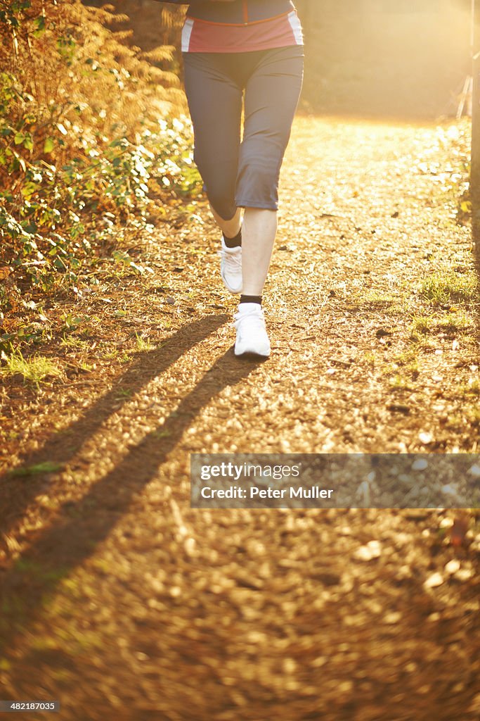 Mature woman jogging on path in sunlight, low section