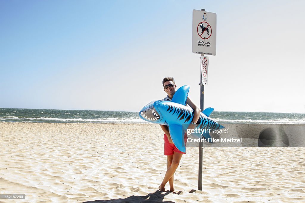 Young man holding inflatable tiger shark, Port Melbourne, Melbourne, Australia