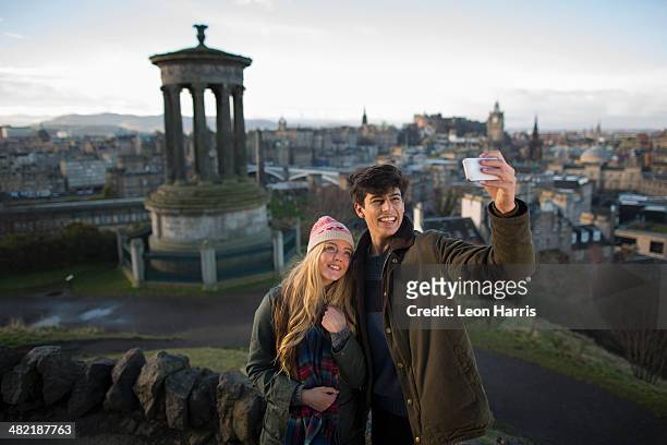 a young couple photograph themselves on calton hill with the background of the city of edinburgh, capital of scotland - edinburgh scotland stockfoto's en -beelden