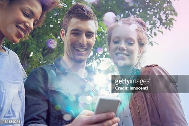 three friends looking at smartphone with lights coming out of it - mobile phone reading low angle stock-fotos und bilder