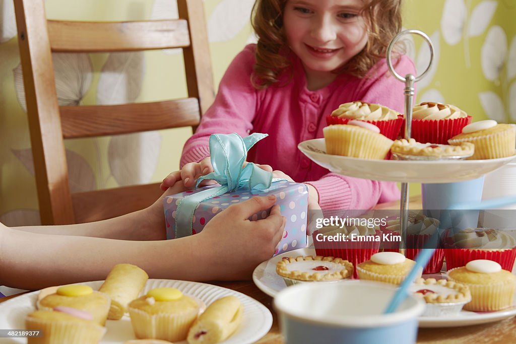 Girl receiving birthday present with cakes on cakestand
