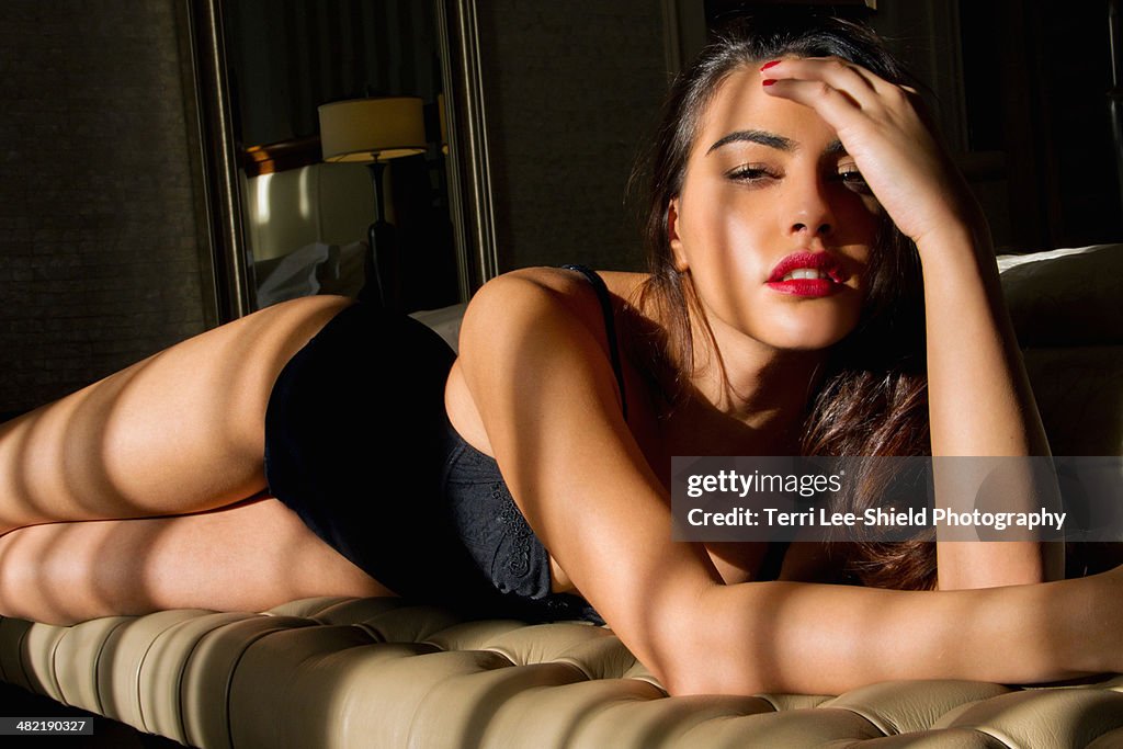 Portrait of sultry young woman reclining on bedroom seat