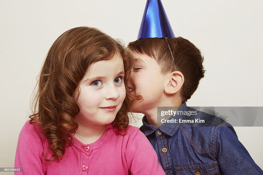 Boy wearing party hat whispering to girl