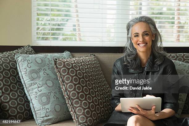 woman using digital tablet on sofa - casaco comprido castanho - fotografias e filmes do acervo