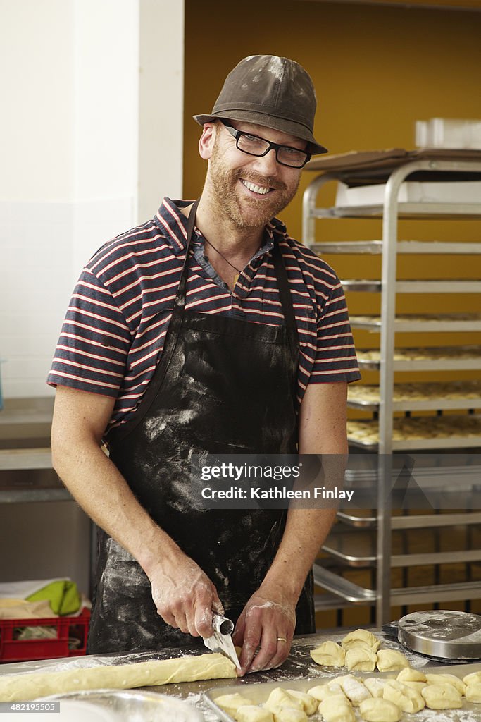 Male baker slicing dough in bakery