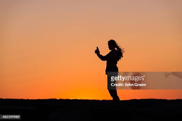 Girl with mobile phone enjoys the sunset from a jetty.