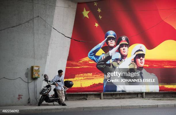 Man waits beside his electric scooter as he charges it next to a Chinese military recruitment poster in Shanghai on July 29, 2015. AFP PHOTO /...