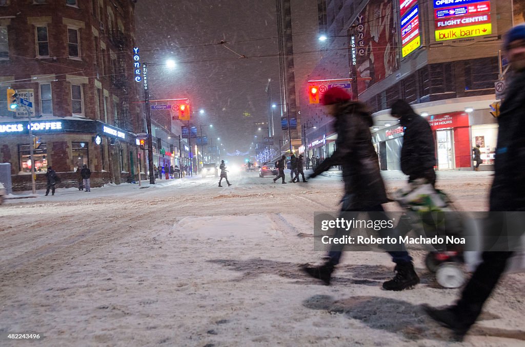 Pedestrians walk the streets of downtown as snow hammers...