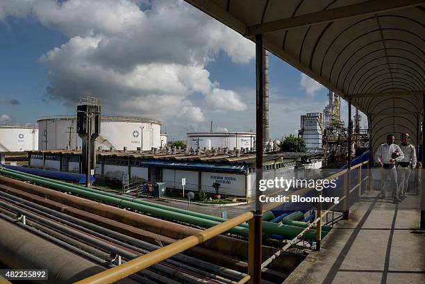 Naphtha tanks stand in the background as workers move along a walkway at the Braskem SA petrochemical plant in Camacari, Brazil, on Tuesday, July 28,...